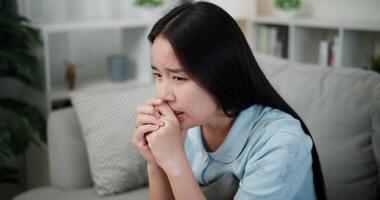 Handheld high angle view shot, Young asian woman sitting alone on the sofa, feeling depressed, lonely, anxious and stressed in the living room at home. Negative emotions video