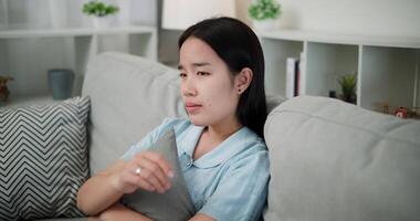 Handheld shot, Young asian woman sitting alone on the sofa, feeling depressed, lonely, anxious and stressed in the living room at home. Negative emotions video