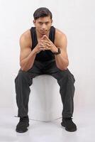 portrait of a man in black tank top sitting on a chair against white background photo