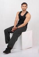 portrait of a young pakistani man in black tank top sitting on a white box photo