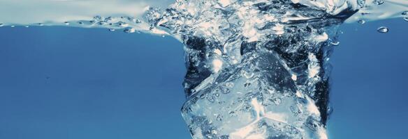 Water splashing and ice cube. Ice splashing into a glass of water. Underwater pouring ice cubes falling into clear watering background. Refreshing chill drinking. Ices in a glass with blue background photo