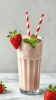 Creamy strawberry smoothie topped with fresh strawberries and mint served in a tall glass with striped straws photo