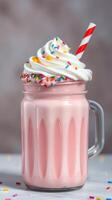 Delicious pink milkshake topped with whipped cream and colorful sprinkles served in a jar photo