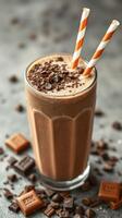 Chocolate milkshake topped with chocolate bits and served with striped straws in a tall glass photo