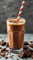 Delicious chocolate milkshake served in a tall glass with a striped straw alongside chocolate pieces photo