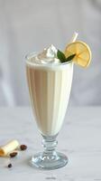 Creamy vanilla shake garnished with lemon slice and mint in a tall glass on a marble surface photo