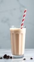 Creamy coffee beverage served in a tall glass with a red and white striped straw against a light backdrop photo