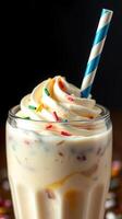 Creamy milkshake topped with colorful sprinkles and a striped straw served in a clear glass photo