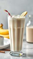 Delicious banana smoothie served in a tall glass with a straw and a slice of banana on the rim photo