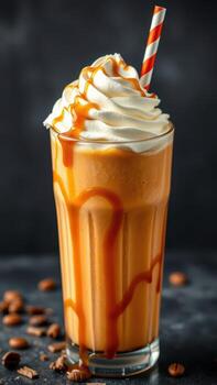 Creamy caramel drink topped with whipped cream and a straw served in a tall glass on a dark surface photo