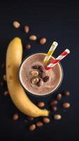 Delicious banana and coffee smoothie topped with nuts and served with colorful straws on a dark background photo