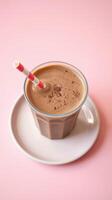 Creamy chocolate drink served in a glass with a colorful straw and plate on a pastel pink surface photo