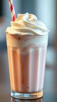 Creamy strawberry milkshake topped with whipped cream and a striped straw served in a glass photo