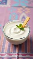 Creamy yogurt served in a glass bowl with a mint leaf and cheese stick on a colorful textile background photo