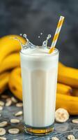 Refreshing banana milkshake with splashes and yellow striped straw on a marble countertop with bananas in the background photo