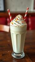 Creamy milkshake topped with colorful sprinkles and two striped straws served in a classic glass photo