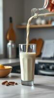 Creamy beverage being poured into a tall glass on a kitchen counter with kitchenware in the background photo