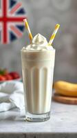 Creamy banana milkshake served in a tall glass with striped straws against a blurred British flag backdrop photo