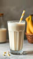 Creamy banana smoothie in a glass with a straw alongside fresh bananas and milk photo