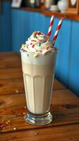 Milkshake topped with whipped cream and colorful sprinkles served in a tall glass at a cozy cafe photo