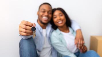New home. Excited black spouses showing keys, sitting in their own house after relocation, focus on key, panorama. Real estate ownership and mortgage loan, buying new flat concept. Shallow depth photo