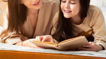 Family hobbies. Mother and daughter reading interesting story together on bed at home photo