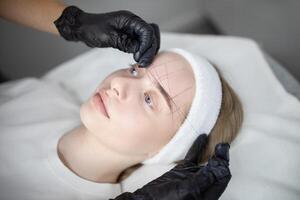 A woman is receiving a long-lasting makeup treatment at a salon. She appears relaxed as a beautician carefully works on her brow area while ensuring precision in the application. photo