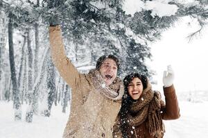 Winter Concept. Joyful Spouses Shaking Branch Making Snowfall Having Fun Standing In Snowy Forest In The Morning. photo