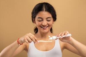 A joyful young Indian woman engages in her skincare routine, applying toothpaste to her toothbrush with a smile. She radiates confidence and beauty in a serene environment. photo