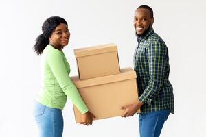 Home Relocation Concept. Joyful black spouses carrying cardboard boxes in their house, young african american couple holding belongings and smiling at camera while moving into new apartment photo