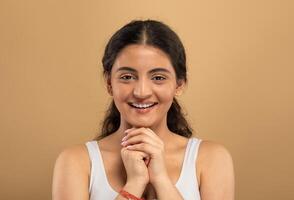 A young Indian woman shows joy while engaging in her skin care routine. She has a warm smile, expressing delight in her pampering session against a neutral background. photo