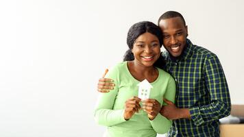 Real Estate Concept. Happy African American Spouses Holding Paper House Figure In Hands And Smiling At Camera, Portrait Of Joyful Young Black Couple Celebrating Buying New Property, Copy Space photo