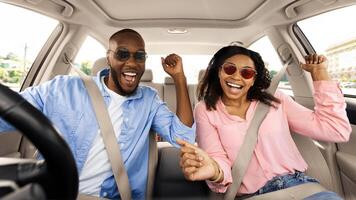 Yes, Summer Vacation Concept. Portrait of excited playful black couple in sunglasses driving car, shaking fists dancing to music enjoying favorite playlist, resting on weekend, windshield view photo