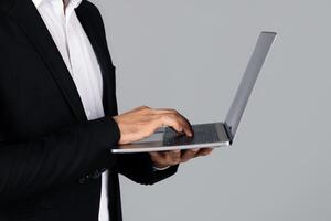 Cropped of entrepreneur stands in a studio environment, focused on typing on a laptop. Dressed in formal attire, he represents a modern, corporate lifestyle. photo