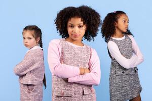 Three preteen girls pose together in a playful manner, displaying diverse expressions and styles. The background is a soft blue, highlighting their unique personalities and the joy of childhood. photo