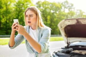 Terrified blonde woman looking for signal after car breakdown, holding smartphone, cannot find mobile network, having difficulty calling roadside assistance. Road problems concept photo