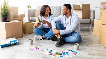 Creative african american spouses working on design for their new house, discussing color palette while sitting on floor among boxes with belongings, thinking about home design, copy space photo