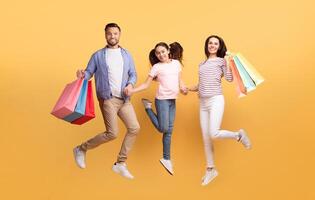A father, mother, and teenage daughter are happily jumping while holding colorful shopping bags. They share smiles and a moment of love against a bright yellow background. photo