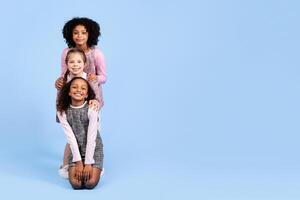 Three joyful girls of different backgrounds are posing together in playful harmony. They are smiling and showcasing a connection that celebrates childhood joy and friendship, copy space photo