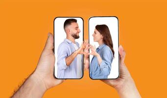 A couple interacts through their smartphones, forming heart shapes with their hands while engaged in a texting conversation. This moment emphasizes their connection despite distance. photo