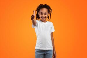 Everything Is Fine. Portrait of happy African American girl showing thumb up, doing approval gesture with finger , smiling, showing that she is good, isolated over yellow studio background photo