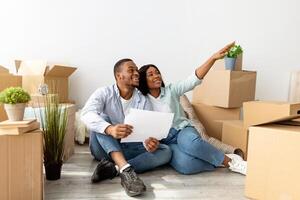 Excited black spouses sitting with laptop and imagining design in their new flat, discussing future home interior together after moving to own house, copy space photo