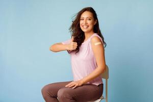 Happy Vaccinated Lady Gesturing Thumbs Up After Vaccination Against Covid-19, Blue Background. Female Patient Showing Like Approving Vaccine For Coronavirus Prevention Concept photo