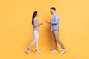 A European couple stands together in a light-filled space, smiling and engaging with each other. They express love and affection while holding their phones, creating a joyful connection. photo