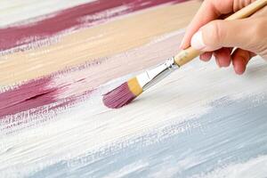 Artist holds a paintbrush, creating an abstract masterpiece with burgundy, beige, and gray tones on a large canvas in a bright studio setting photo