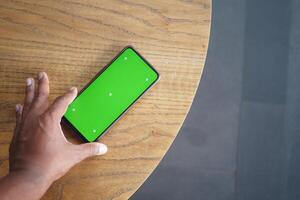 A hand reaches for a smartphone with a green screen on a table photo