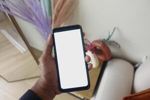 A hand holds a smartphone with a blank screen in a cozy setting photo