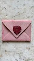Pink envelope sealed with red heart shaped wax seal on white background photo