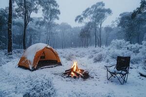 Camping tent glowing in snowy woods at dusk with burning campfire photo