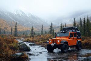 Orange off-road vehicle crossing shallow river in autumn mountains photo